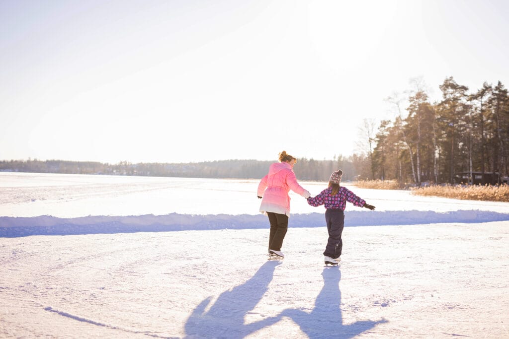 aurinkoisella säällä luistelu, aikuinen ja lapsi käsikädessä